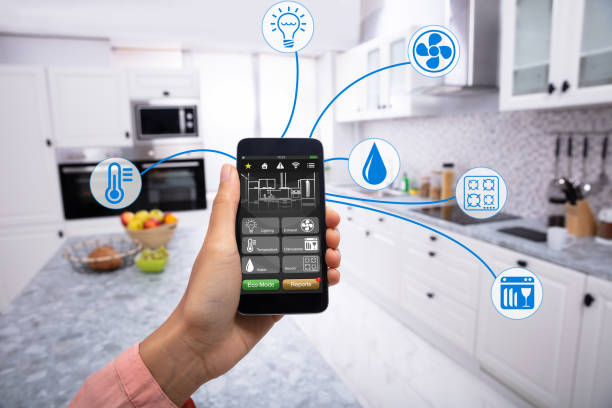 Woman's Hand Using Home Control System On Cellphone With Various Icons In The Kitchen